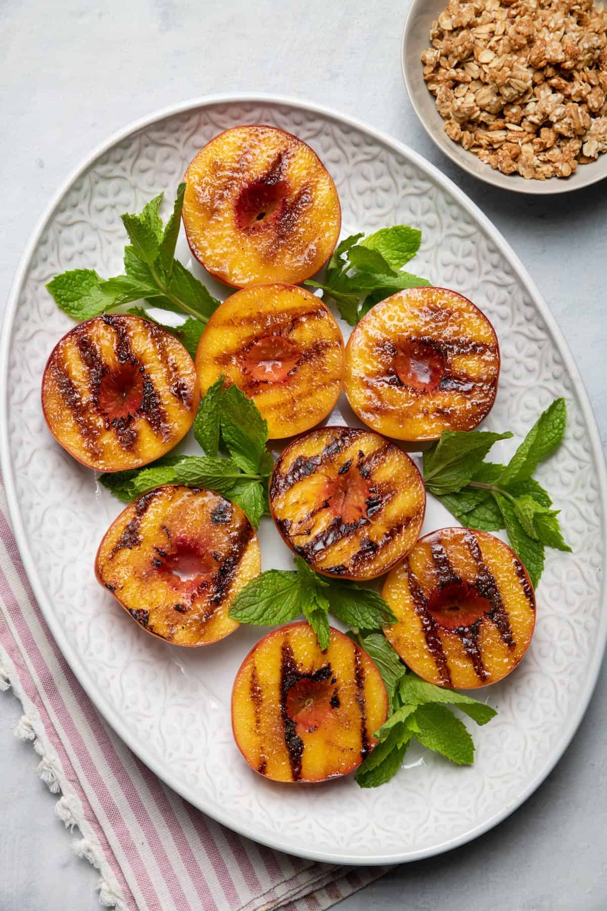 Platter of grilled peaches served with fresh mint and granola on the side