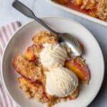 Peach crisp in a bowl served with two scoops of vanilla ice cream