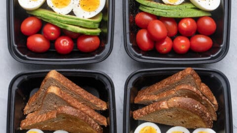 4 meal prep containers with the avocado, egg, toast and tomatoes