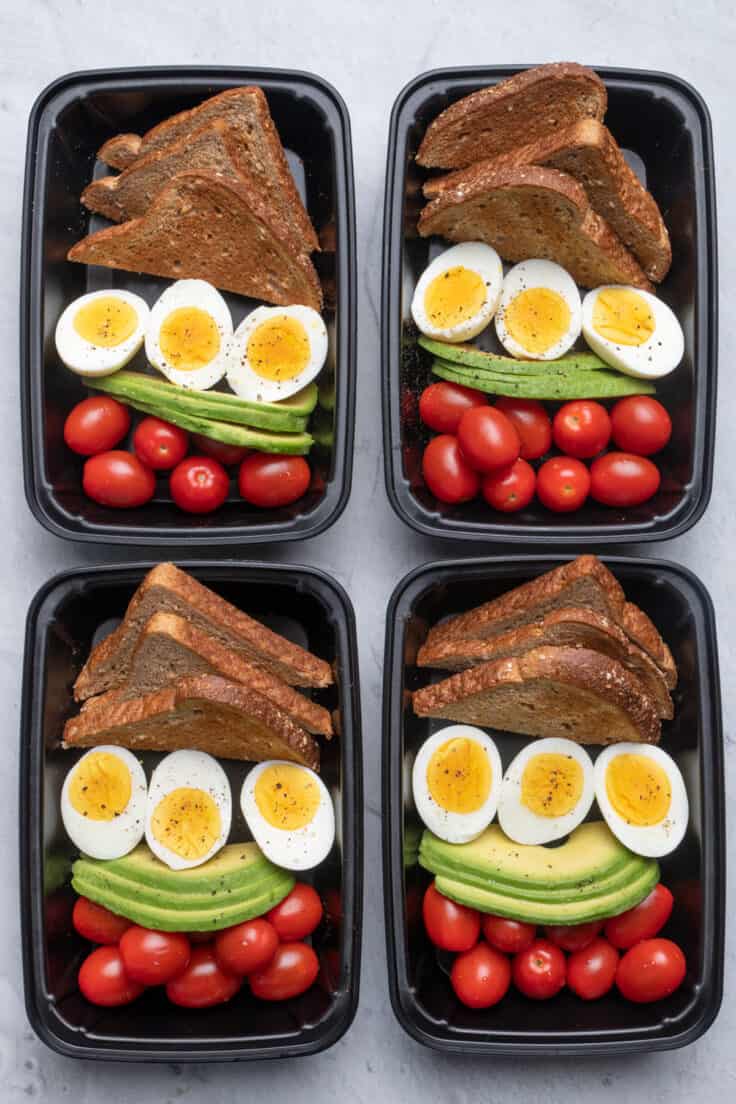 4 meal prep containers with the avocado, egg, toast and tomatoes