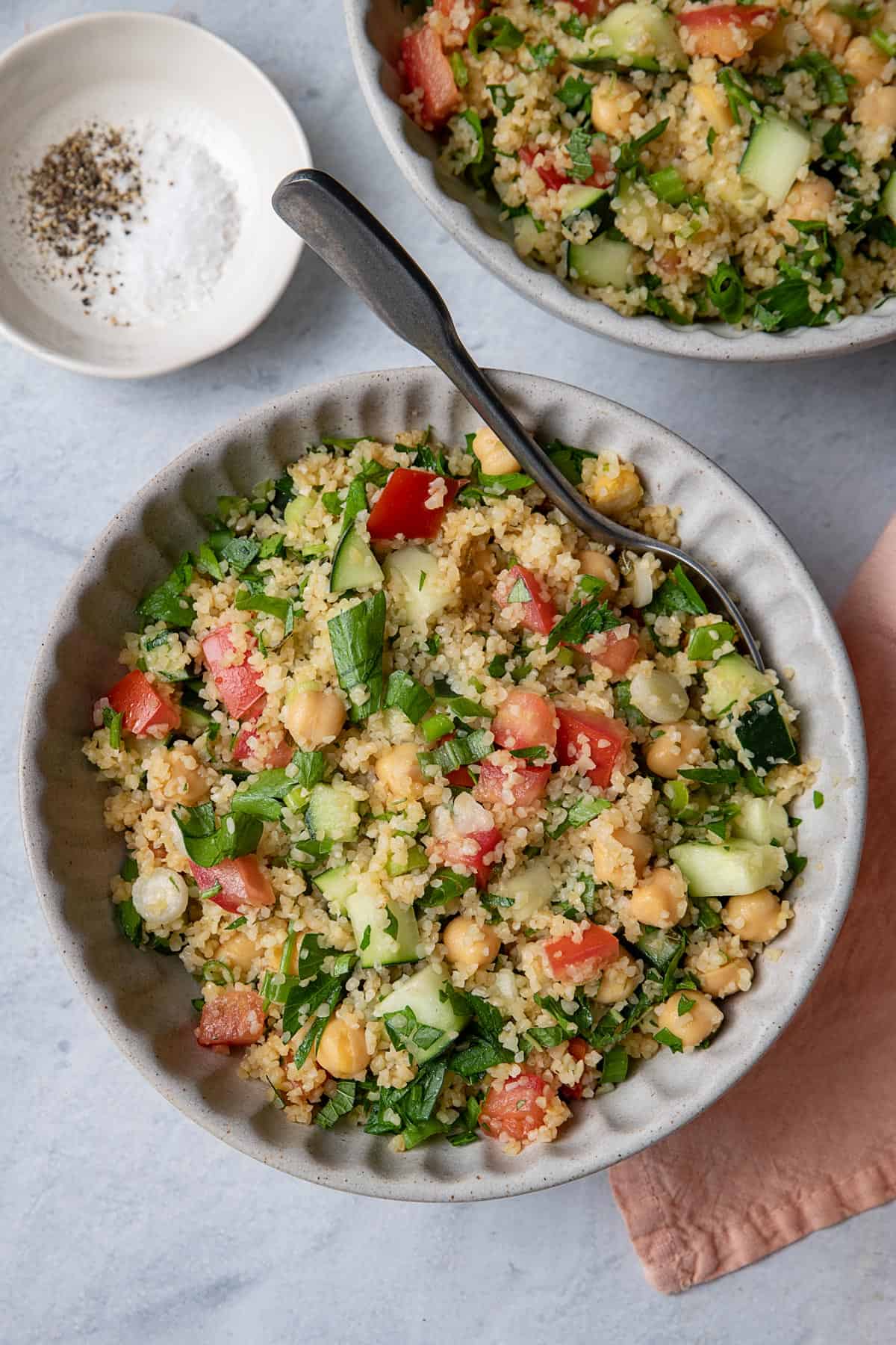 Two bowls of the bulgur chickpea salad with pinch bowl next to them