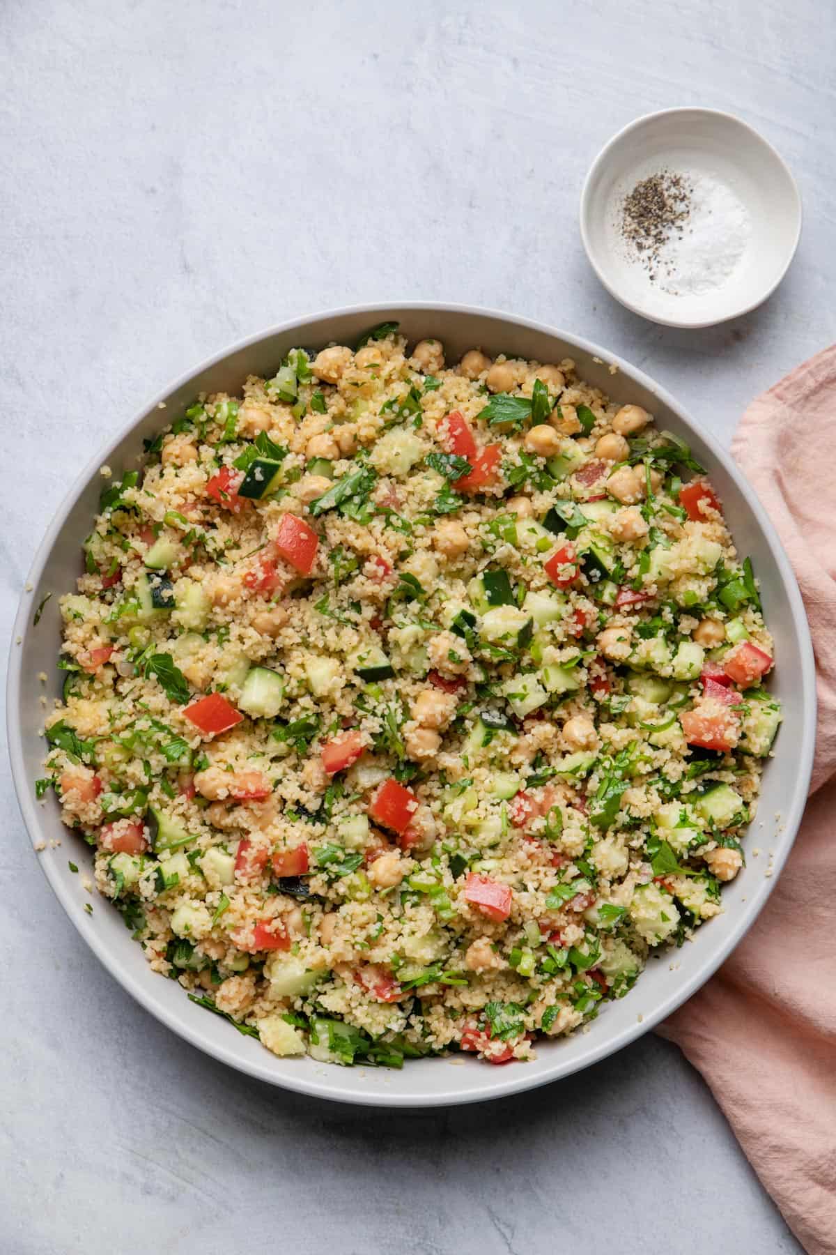 Large bowl of bulgur salad with salt and pepper in pinch bowl to it