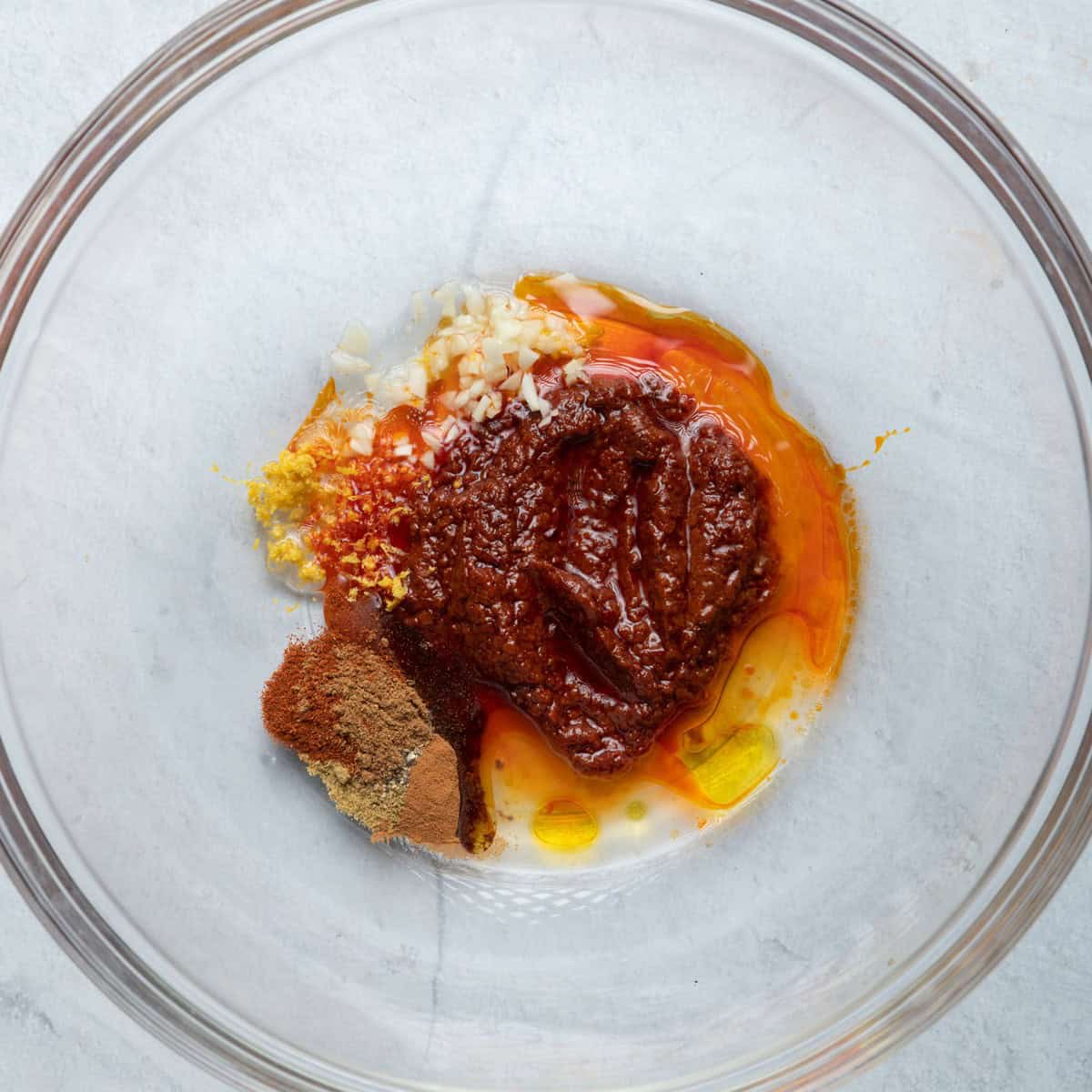 Olive oil, harissa, garlic, paprika, cumin, salt and pepper in a bowl before combining.