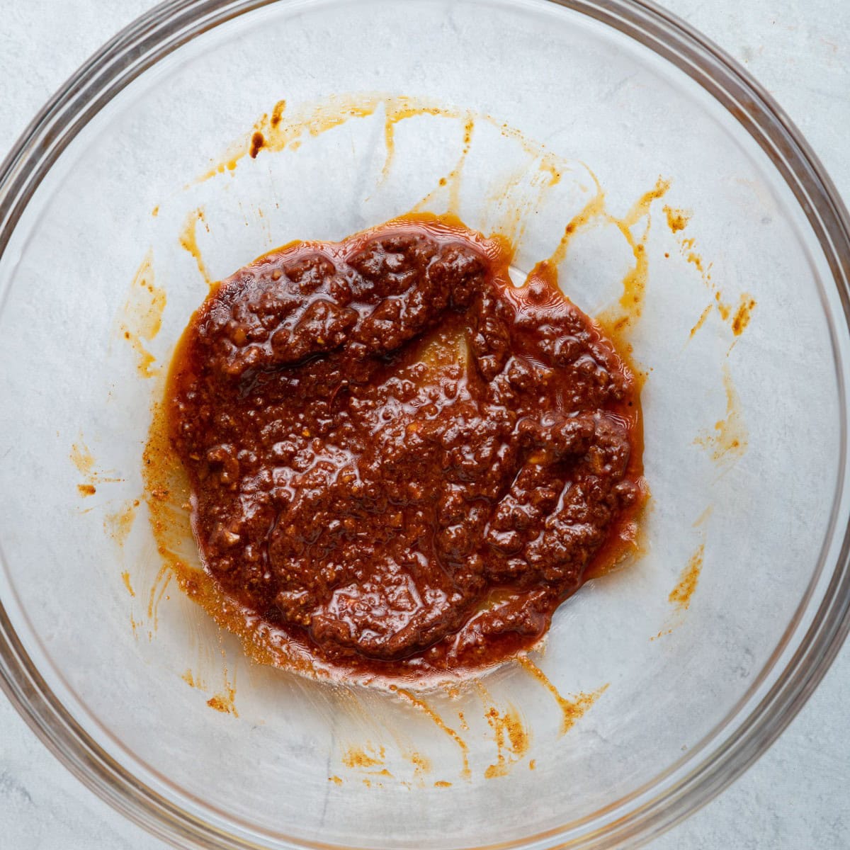 Olive oil, harissa, garlic, paprika, cumin, salt and pepper in a bowl after combining.