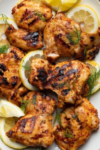 Grilled harissa chicken on serving dish with lemon slices.