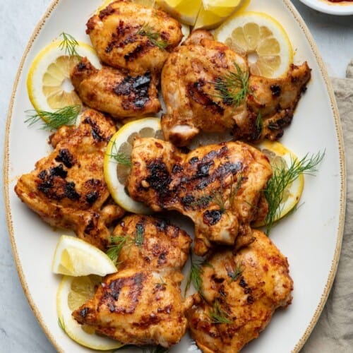 Grilled harissa chicken on serving dish with lemon slices.