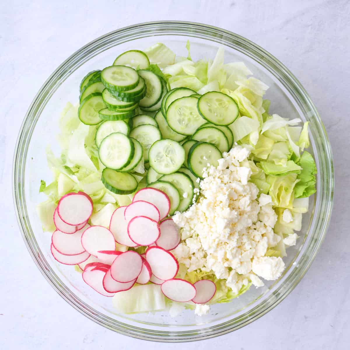 Iceberg, cucumbers, radishes and feta added on top in the same bowl.