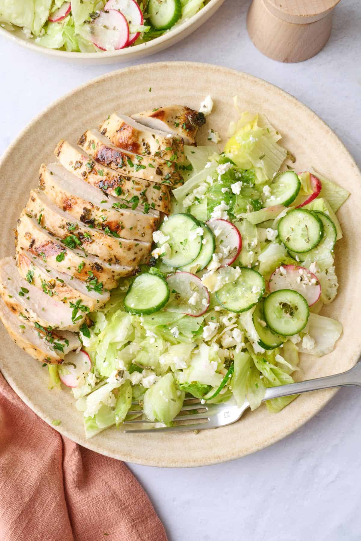 Serving of salad on a plate with sliced grilled lemon chicken, and the serving bowl of salad nearby.