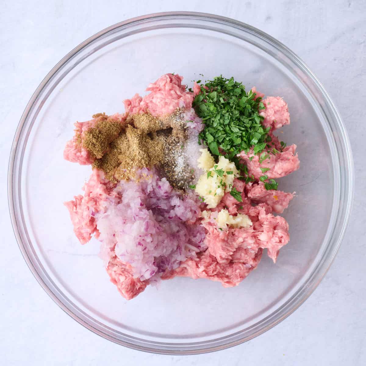 Ground lamb, grated red onion, garlic, parsley, cumin, coriander, salt, and black pepper in a large bowl before combining.