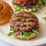 Assembled burgers on a platter topped with yogurt, lid off one burger, and yogurt dish nearby.