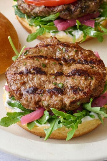 Assembled burgers on a platter topped with yogurt, lid off one burger, and yogurt dish nearby.