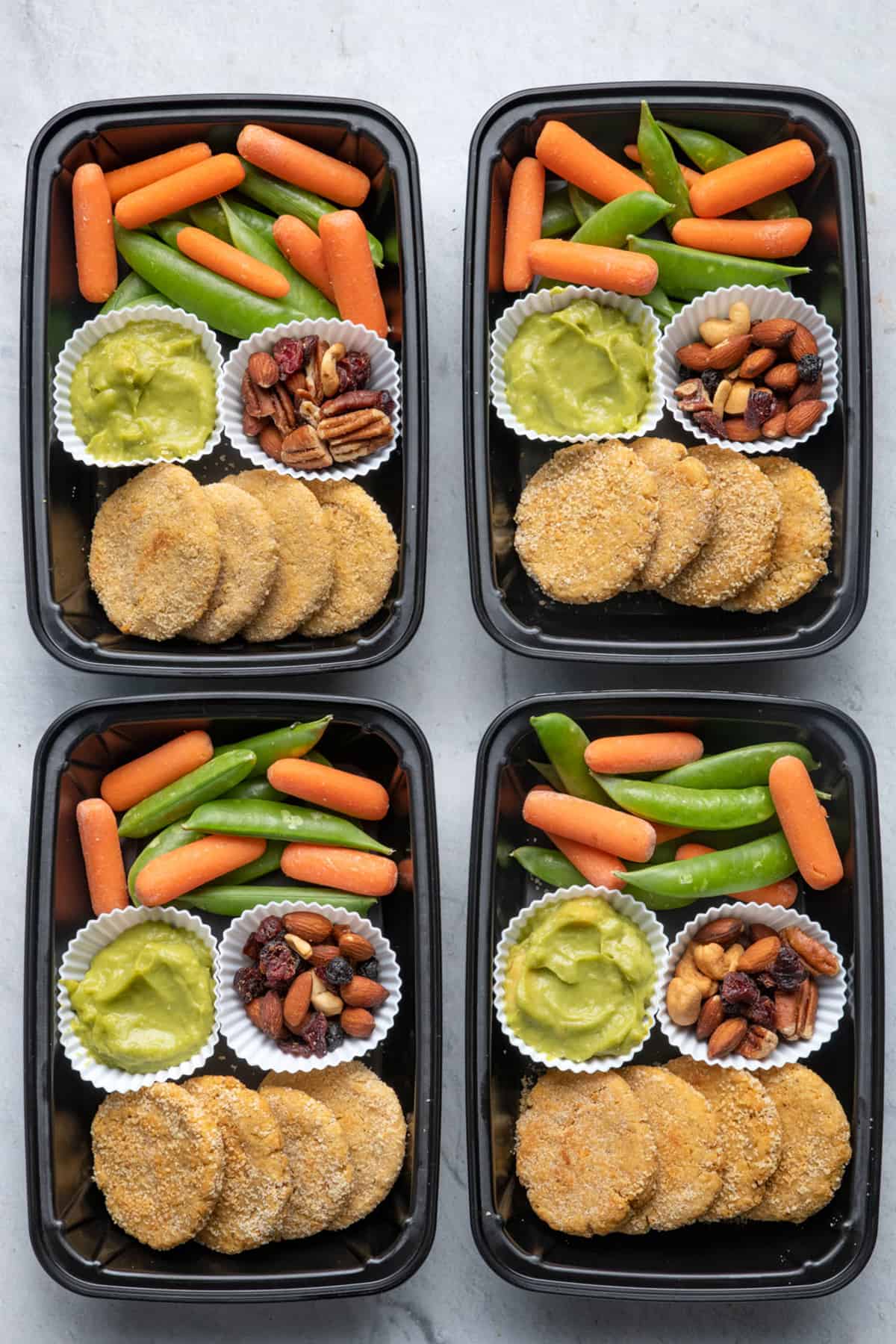 4 meal prep containers with the chickpea bites and avocado dip along with veggies and trail mix