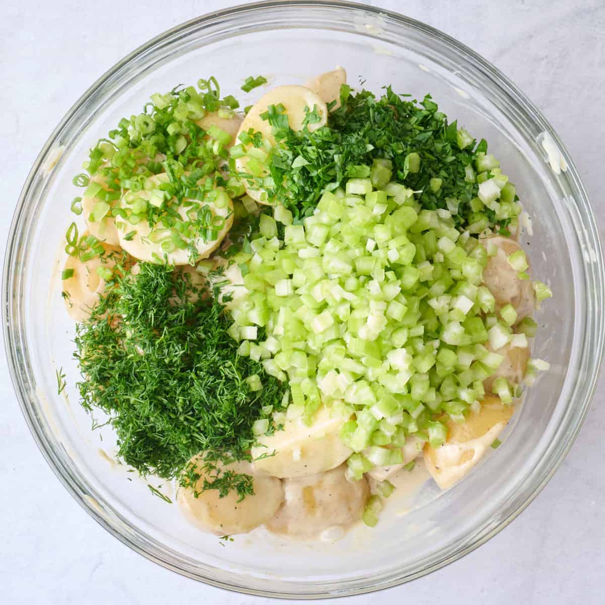 Celery, green onions and herbs added to the bowl, before combining.