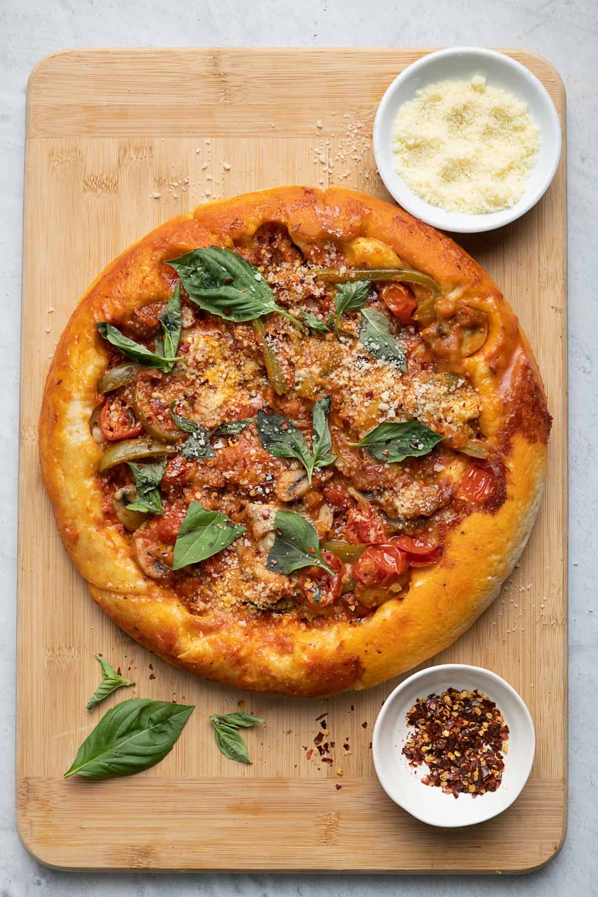 Upside down pizza on cutting board with parmesan cheese, crushed red pepper and basil