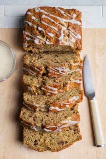 Sliced lemon zucchini bread on board with knife next to it and bowl of glaze