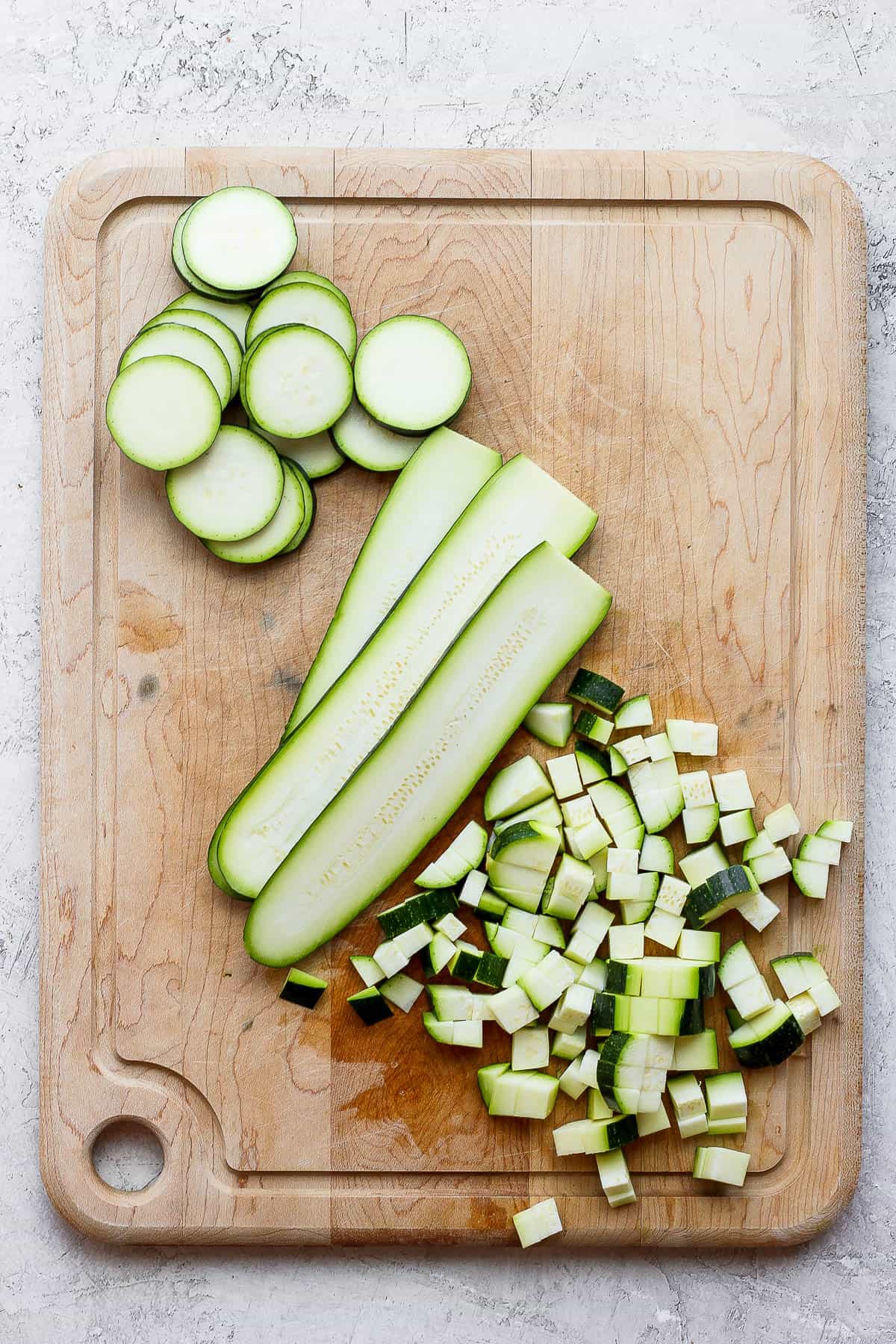 Chopped zucchini three different ways on a butting board