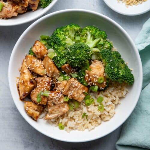 Two bowls of the chicken teriyaki bowls garnished with scallions and sesame seeds.