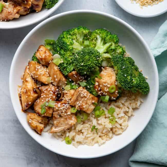 Two bowls of the chicken teriyaki bowls garnished with scallions and sesame seeds.