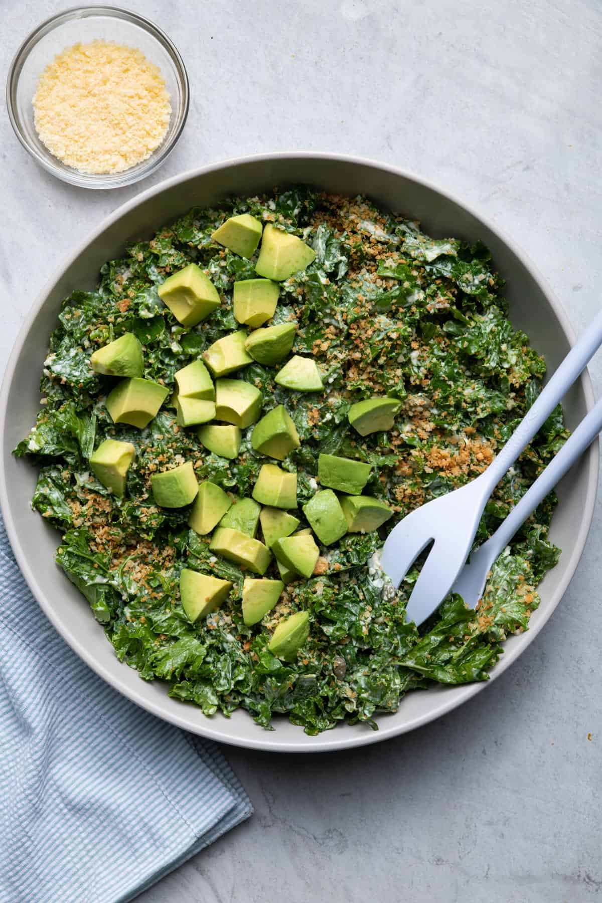 Large serving bowl of kale caesar salad topped with garlic breadcrumbs and avocados