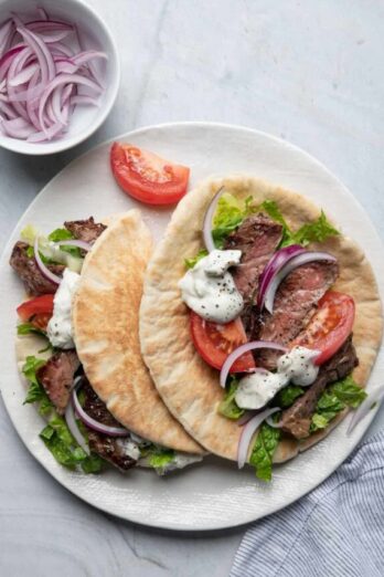 Two steak gyros on a plate with toppings