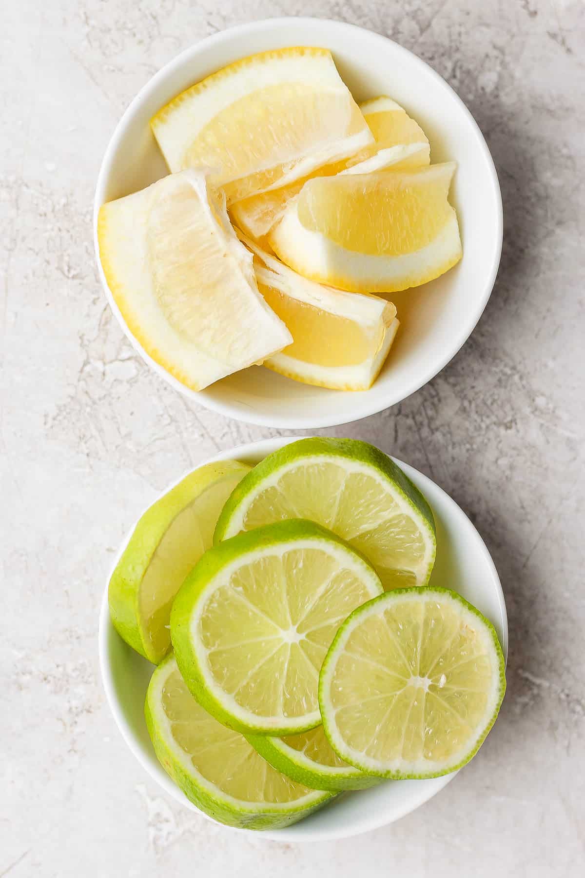 Two bowls of lime slices and lemon wedges