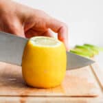 Large lemon on cutting board getting cut with large knife
