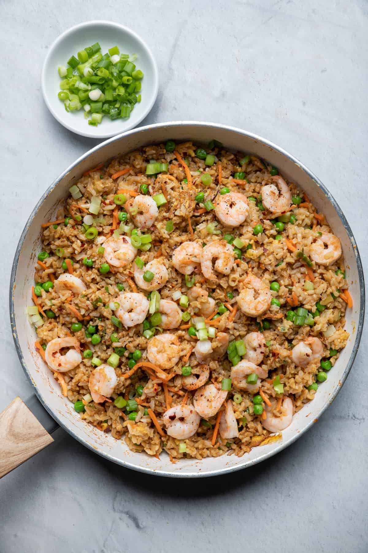 Large pan of shrimp fried rice with green onions on the side