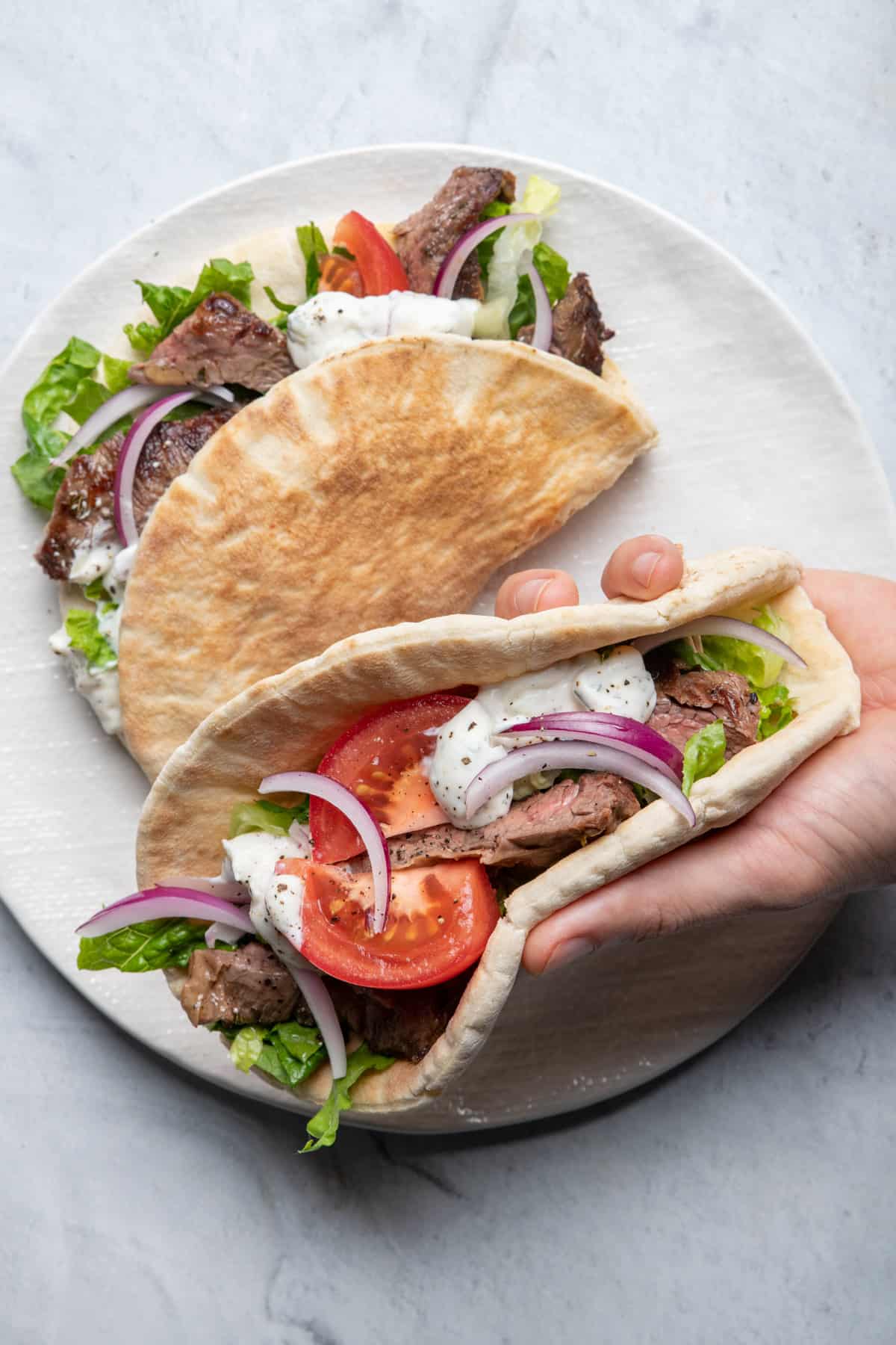 Hand hold steak gyro assembled on pita with toppings