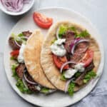 Two steak gyros on a plate with toppings