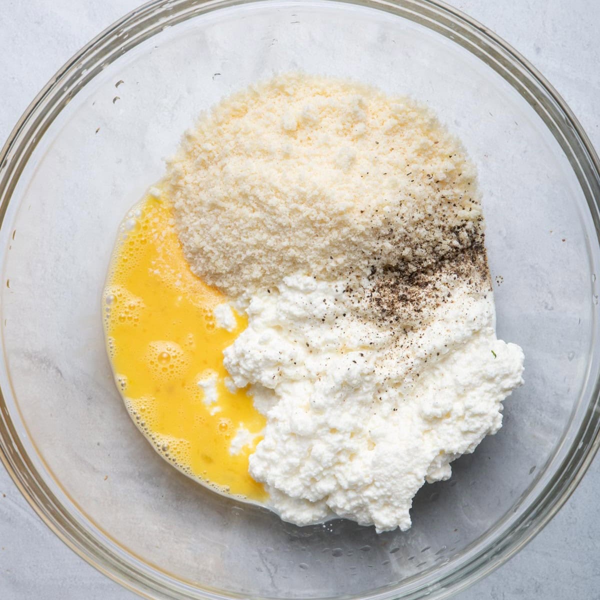 Bowl with egg, ricotta, parmesan, basil and pepper before mixing.