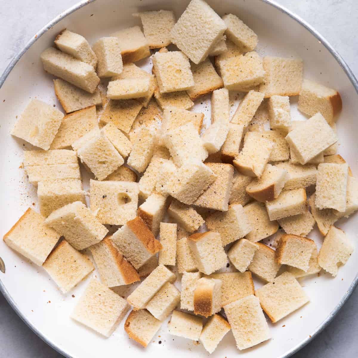 Bread cubes on skillet with salt, pepper, garlic powder and olive oil before cooked.