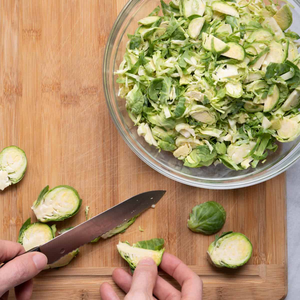 Brussel sprout cut in half with knife slicing it and other sliced ones around cutting board.