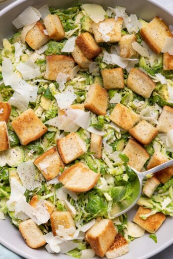 Large bowl of the salad with croutons and parmesan cheese with spoon or tongs for serving in the bowl.