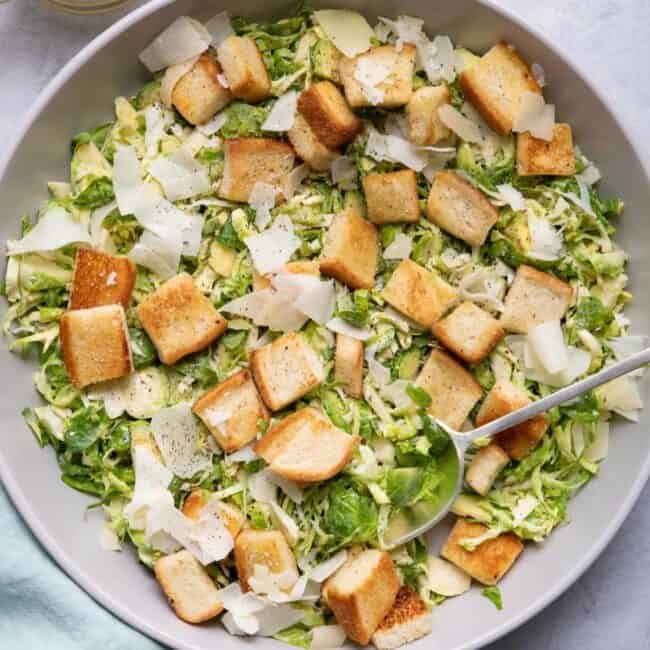 Large bowl of the salad with croutons and parmesan cheese with spoon or tongs for serving in the bowl.