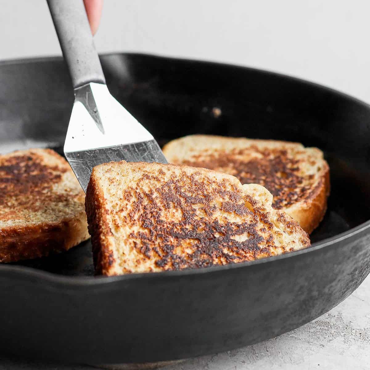 Three pieces of cooked french toast in a skillet, with one being removed.