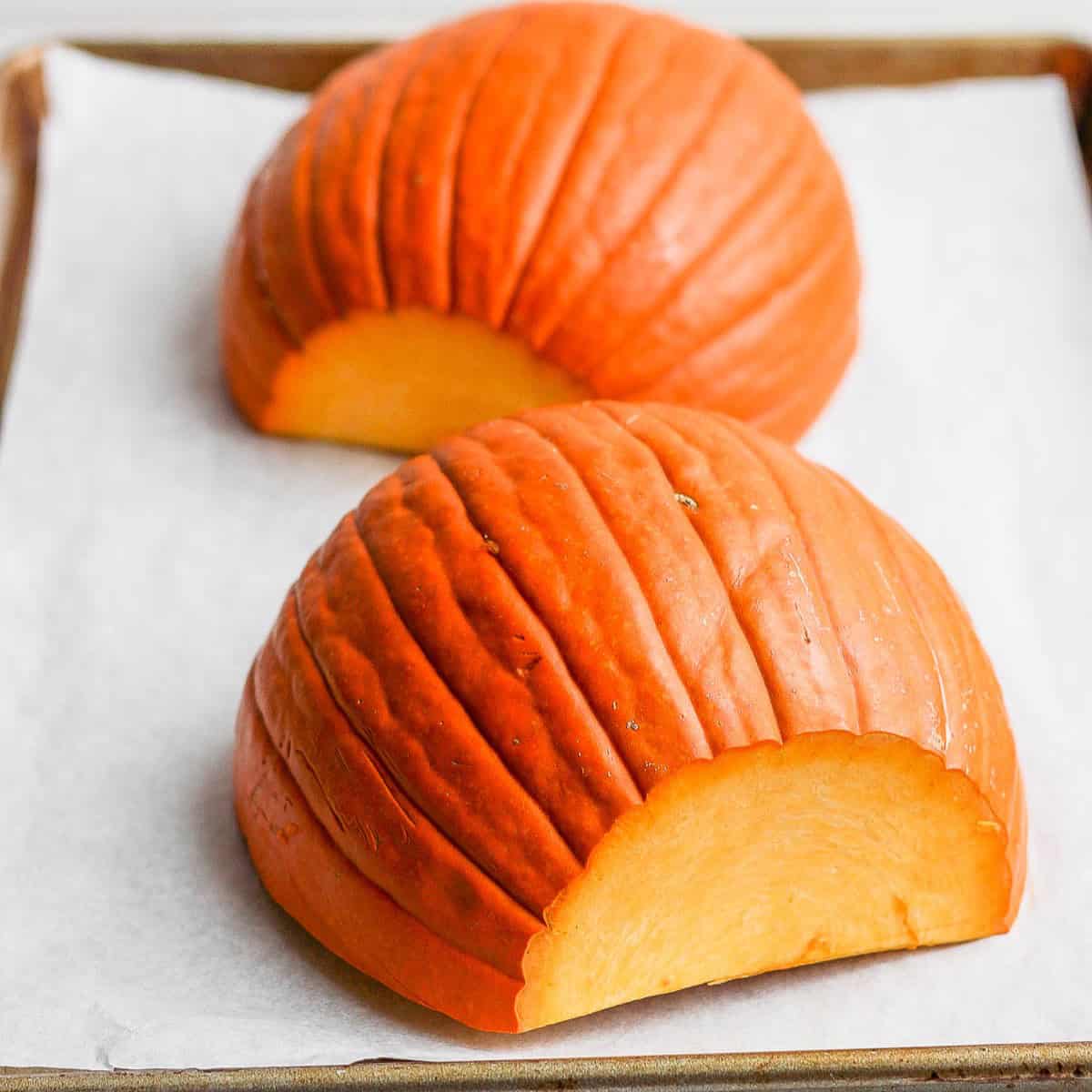 Two pumpkin halves flesh side down on baking sheet lined with parchment paper.