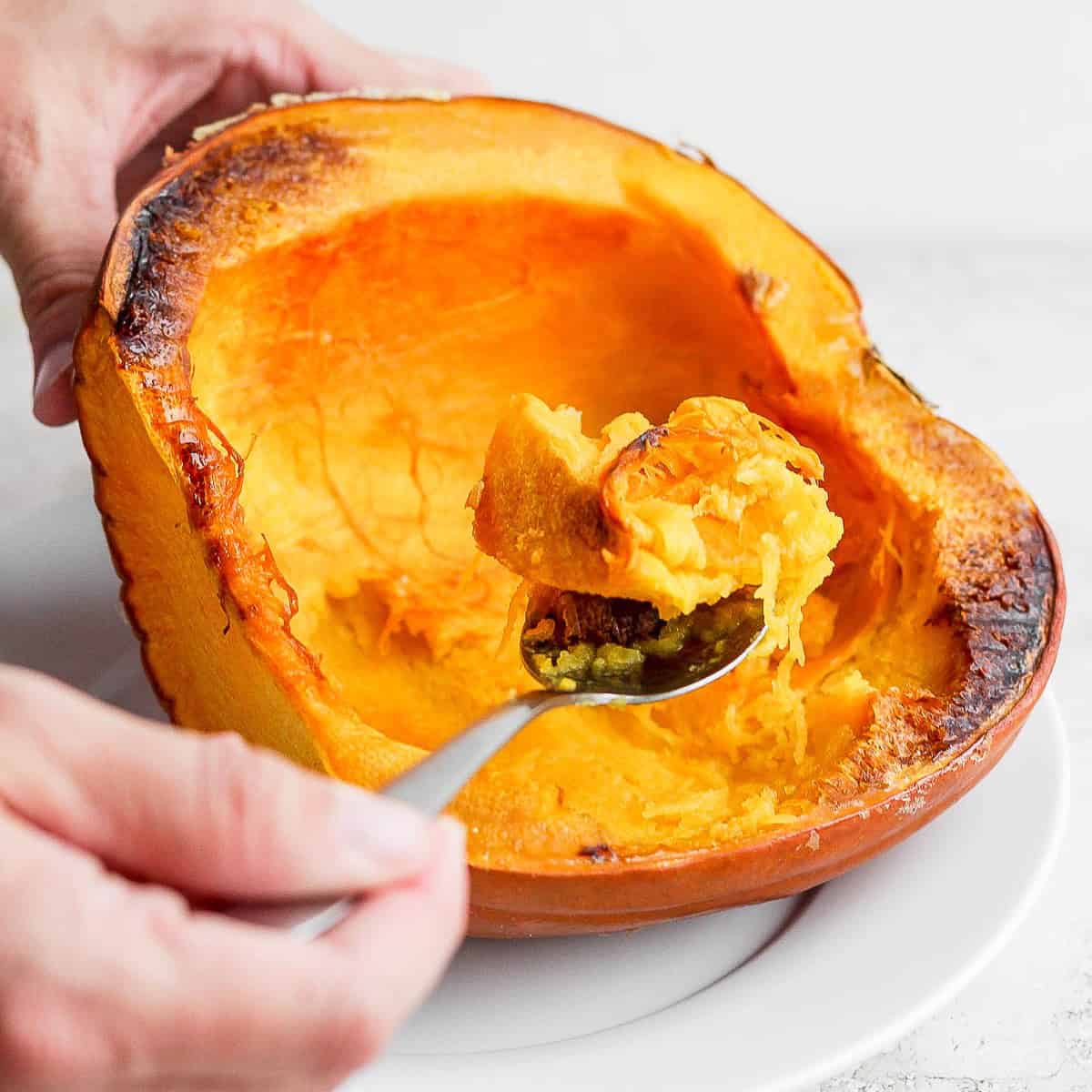 Using spoon to remove cooked flesh from pumpkin halves.