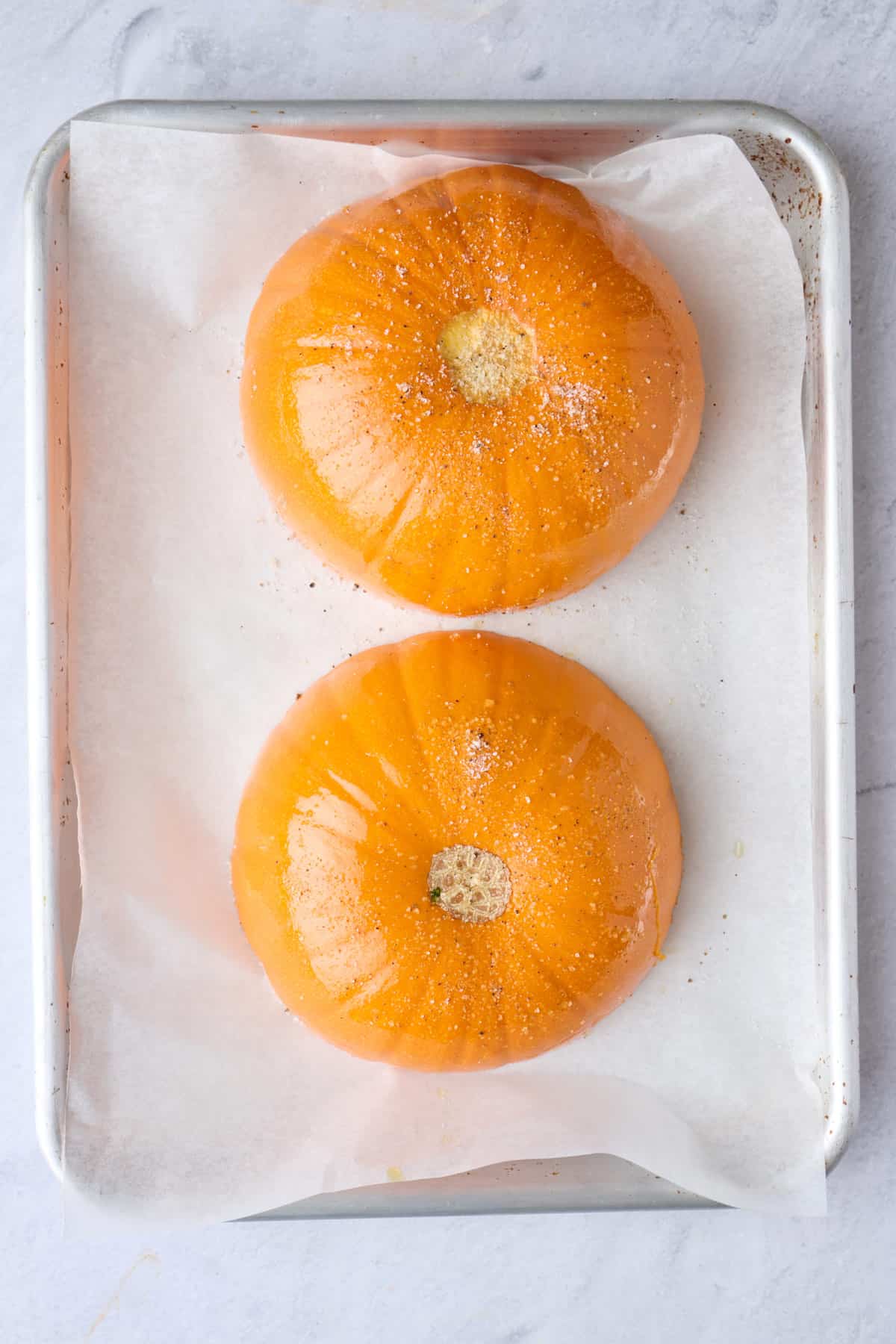 Seasoned pumpkin cut side down on a small baking sheet.