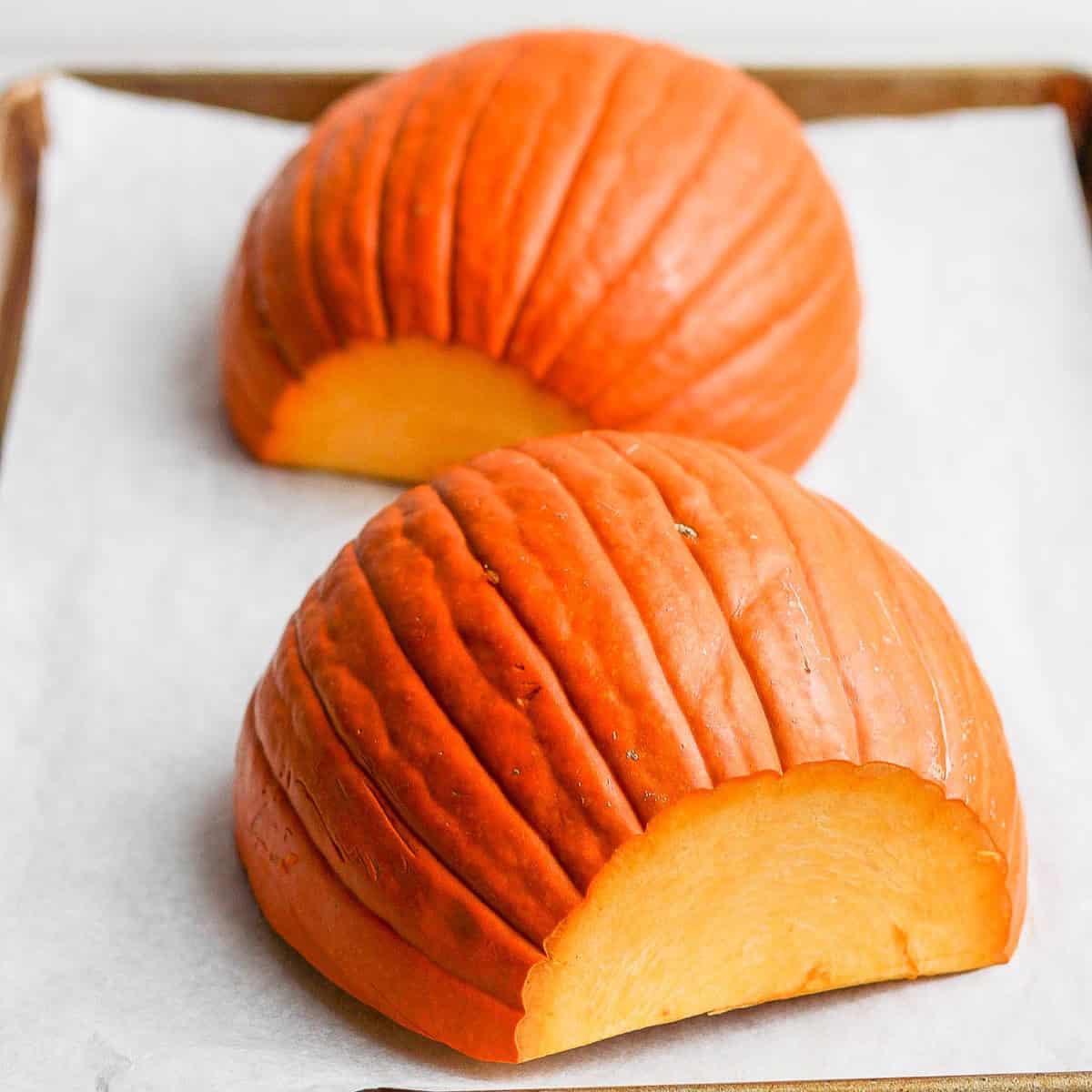 Two pumpkin halves flesh side down on baking sheet lined with parchment paper.