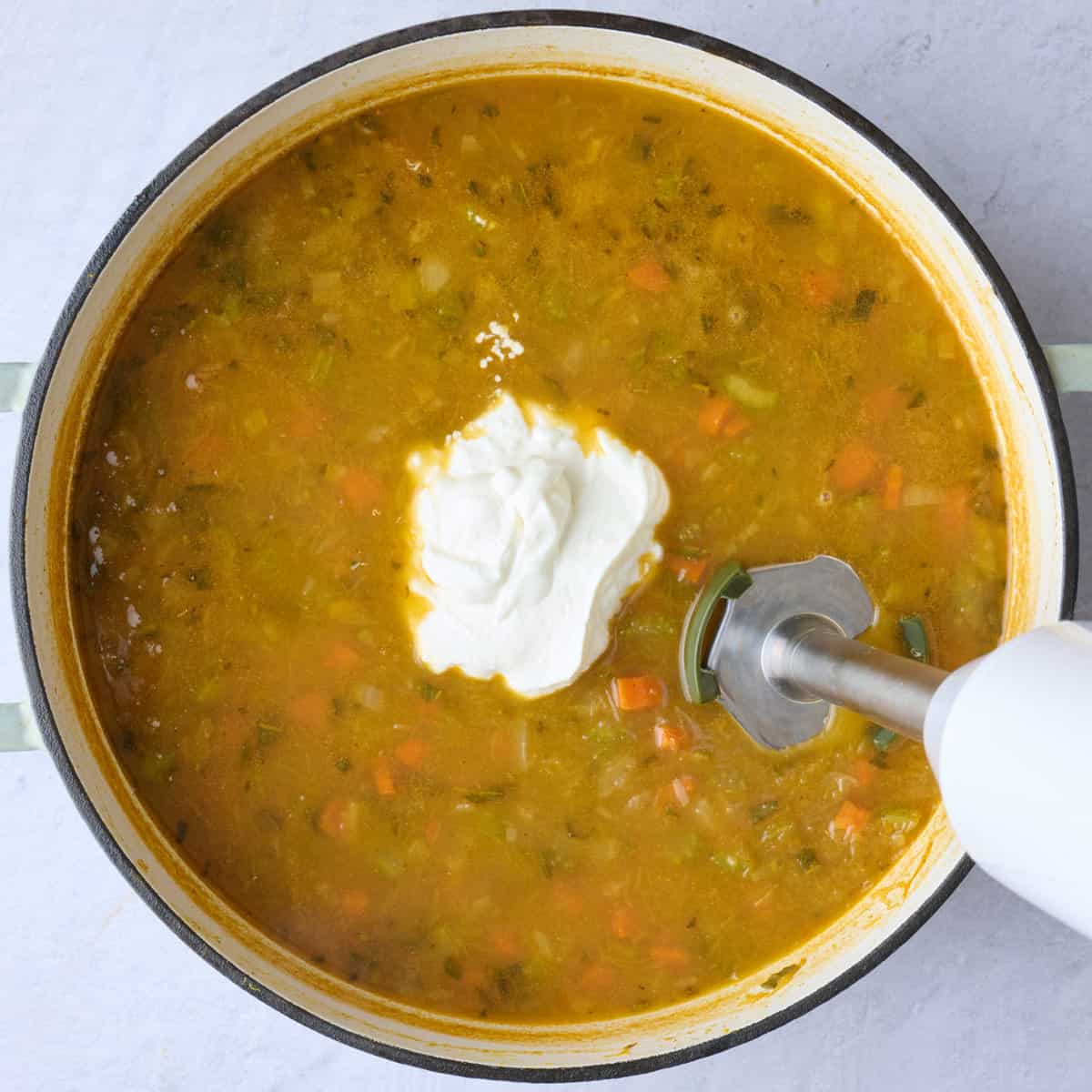 Yogurt added to the soup and an immersion blender blending it.