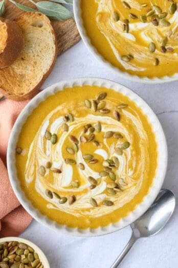 Two bowls of pumpkin soup garnished with an extra swirl of yogurt and pumpkin seeds.