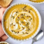 Two bowls of pumpkin soup garnished with an extra swirl of yogurt and pumpkin seeds.