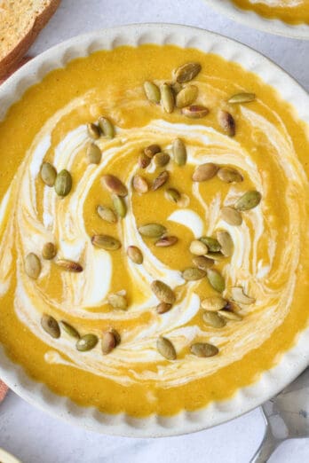 Two bowls of pumpkin soup garnished with an extra swirl of yogurt and pumpkin seeds.