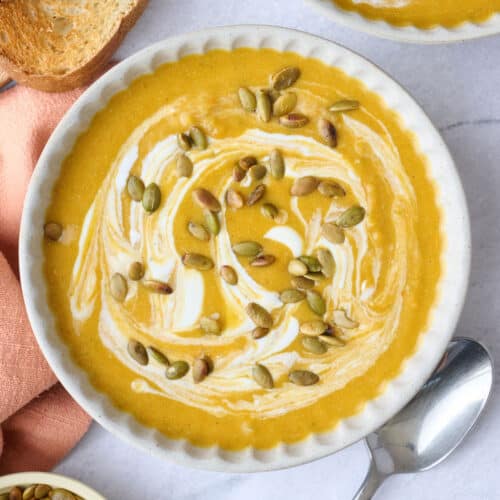 Two bowls of pumpkin soup garnished with an extra swirl of yogurt and pumpkin seeds.