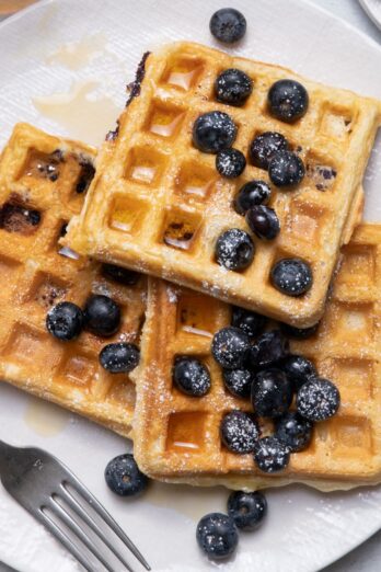 Plate of waffles with blueberries, powdered sugar and maple syrup on top.