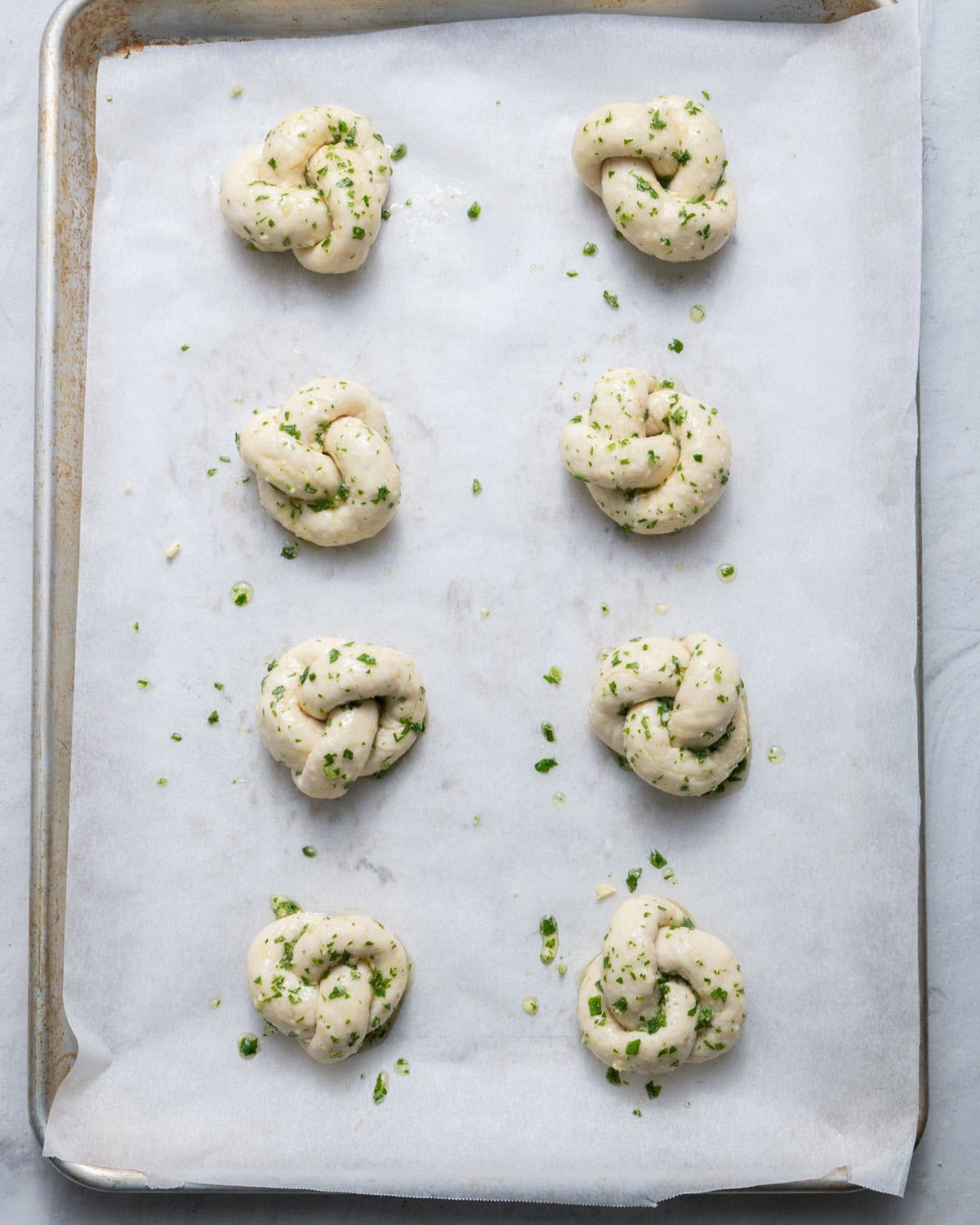 Baking sheet with 8 garlic knots before baking brushed with the olive oil mixture.