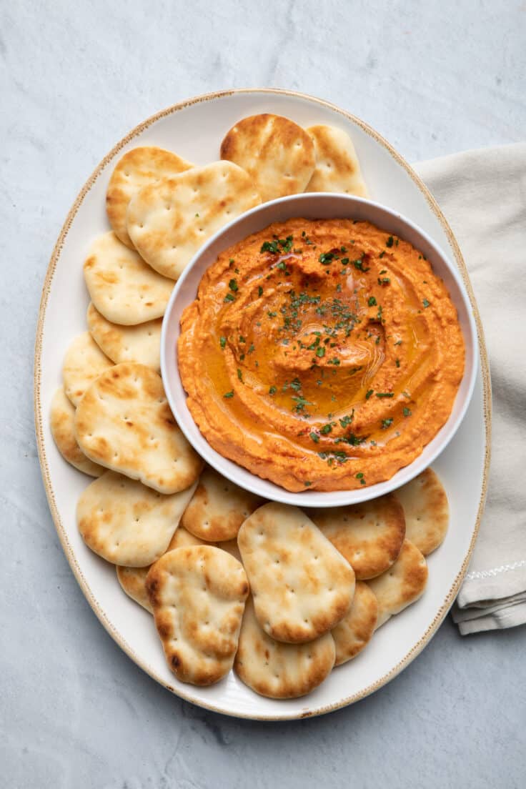 Roasted red pepper hummus on a platter served with small naan dippers