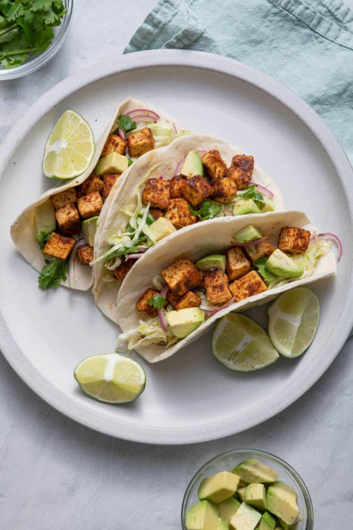 Tofu tacos on a plate topped with coleslaw with limes