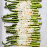 Oven roasted asparagus on parchment paper with melty cheese on top