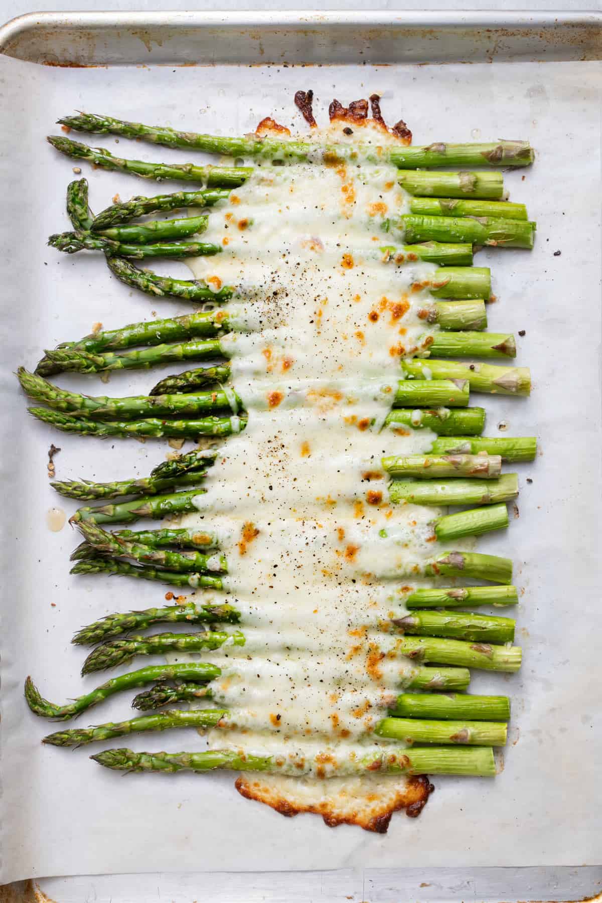 Oven roasted asparagus on parchment paper with melty cheese on top